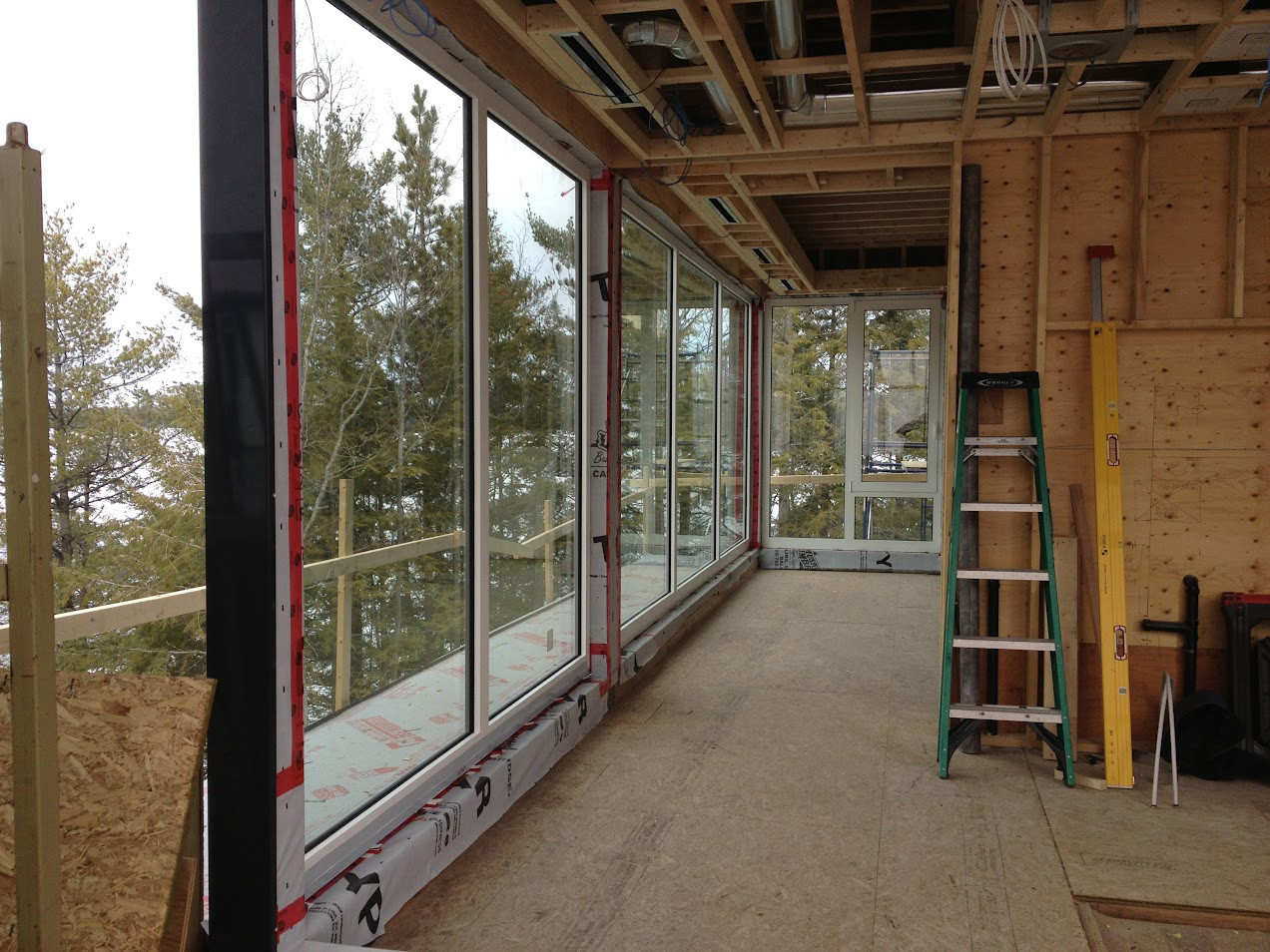 Completed installation at a Muskoka cottage featuring Reynaers Aluminum MasterLine 8 large fixed glazing and tilt-turn windows, framing forest views through expansive glass walls.