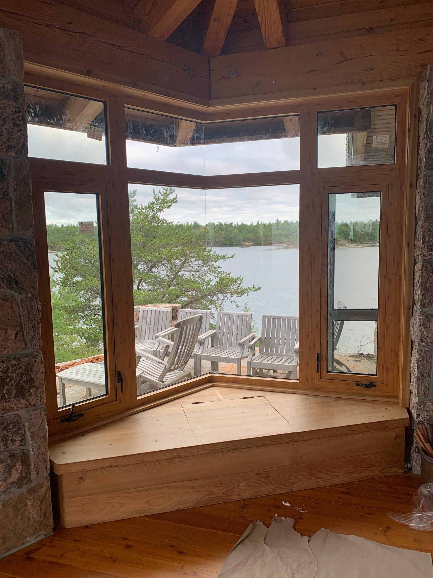 Interior view of Reynaers CS77 open corner windows with wood sublimation finish, overlooking water and trees from a Georgian Bay island cottage.