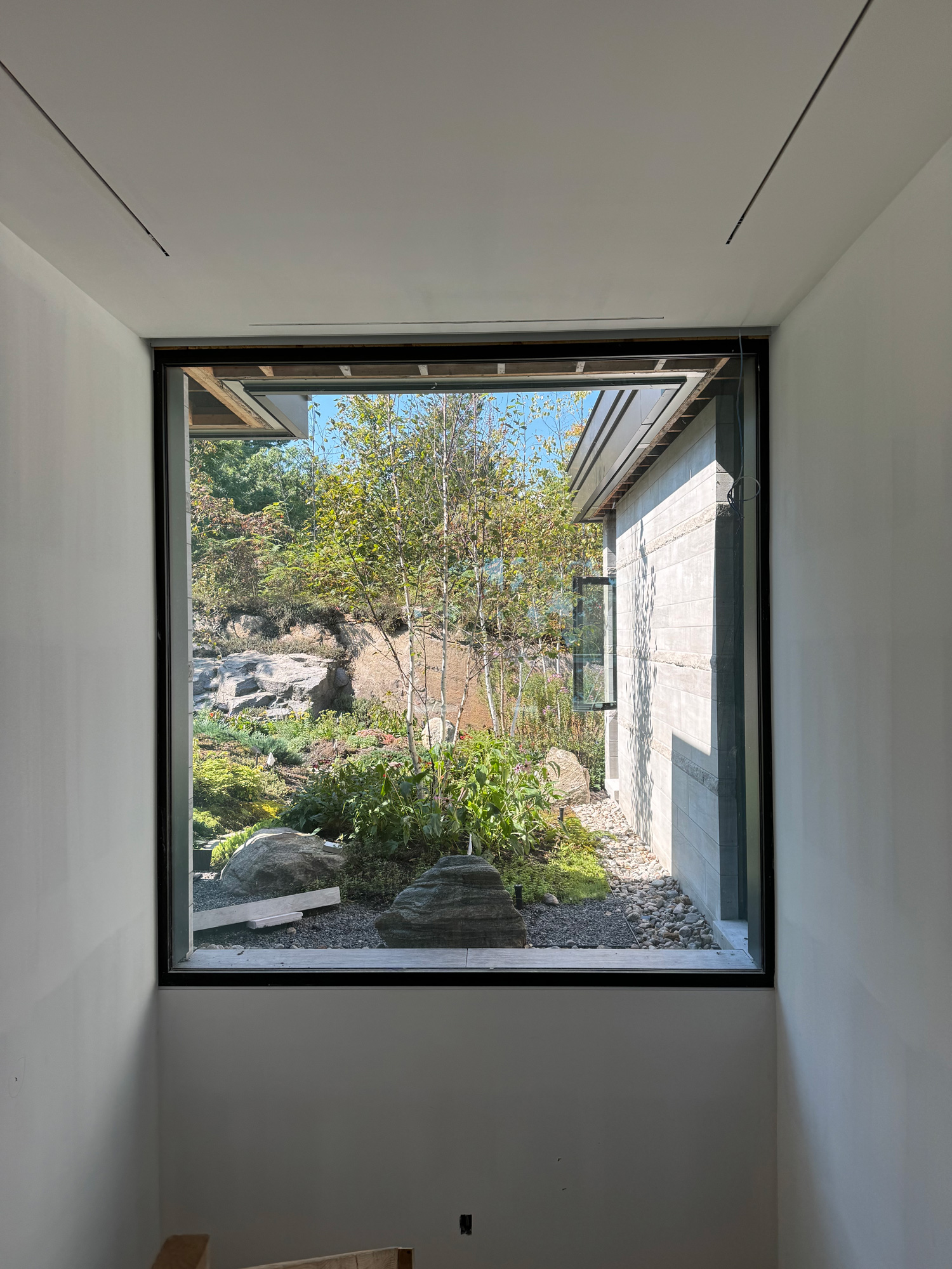 Interior view of a stairwell at a St. Lawrence River home featuring a large Reynaers Aluminum window, framing landscaped stone and garden views with modern glazing.