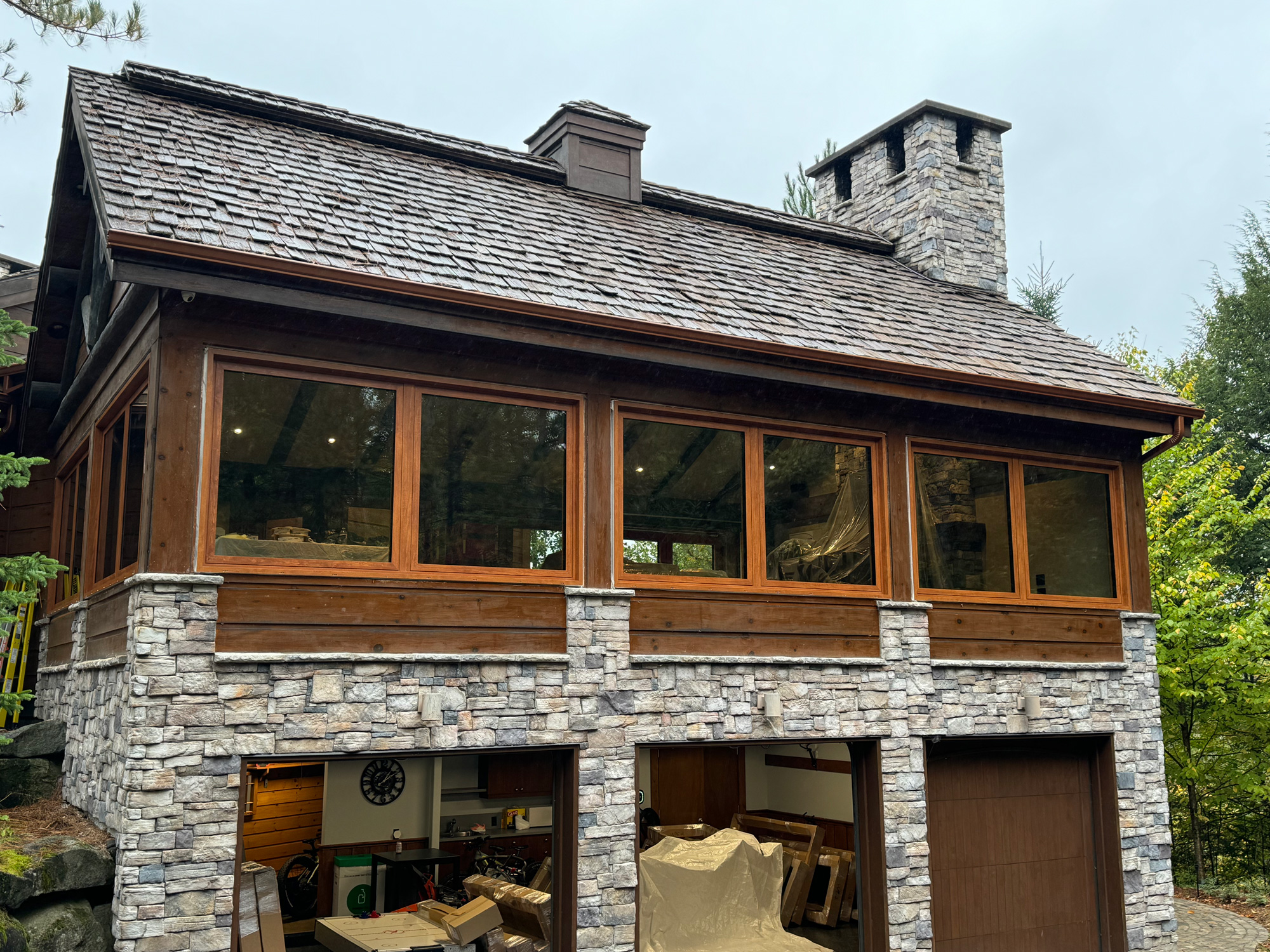 Exterior view of a Mont Tremblant cottage wall featuring Reynaers Masterline 8 windows with wood sublimation finish, blending modern performance with rustic stone and timber.