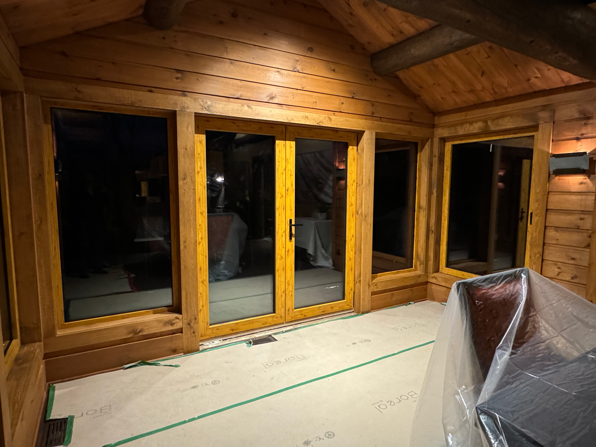 Evening view of a cottage interior featuring Reynaers Aluminum MasterLine 8 French door with surrounding fixed and operable windows in a timber-clad wall.
