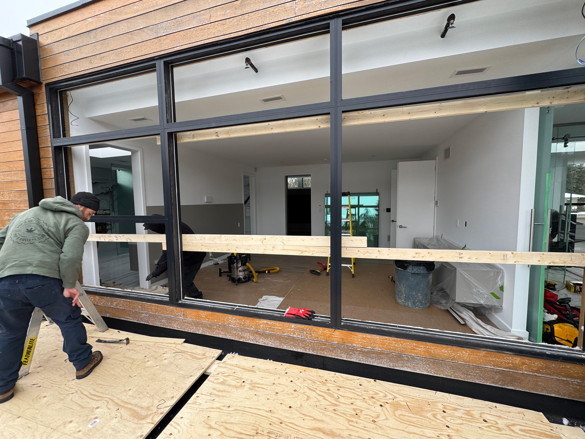 Crew installing Reynaers MasterLine 8 windows in a Muskoka cottage, with black aluminum framing set into a wood-clad exterior wall.