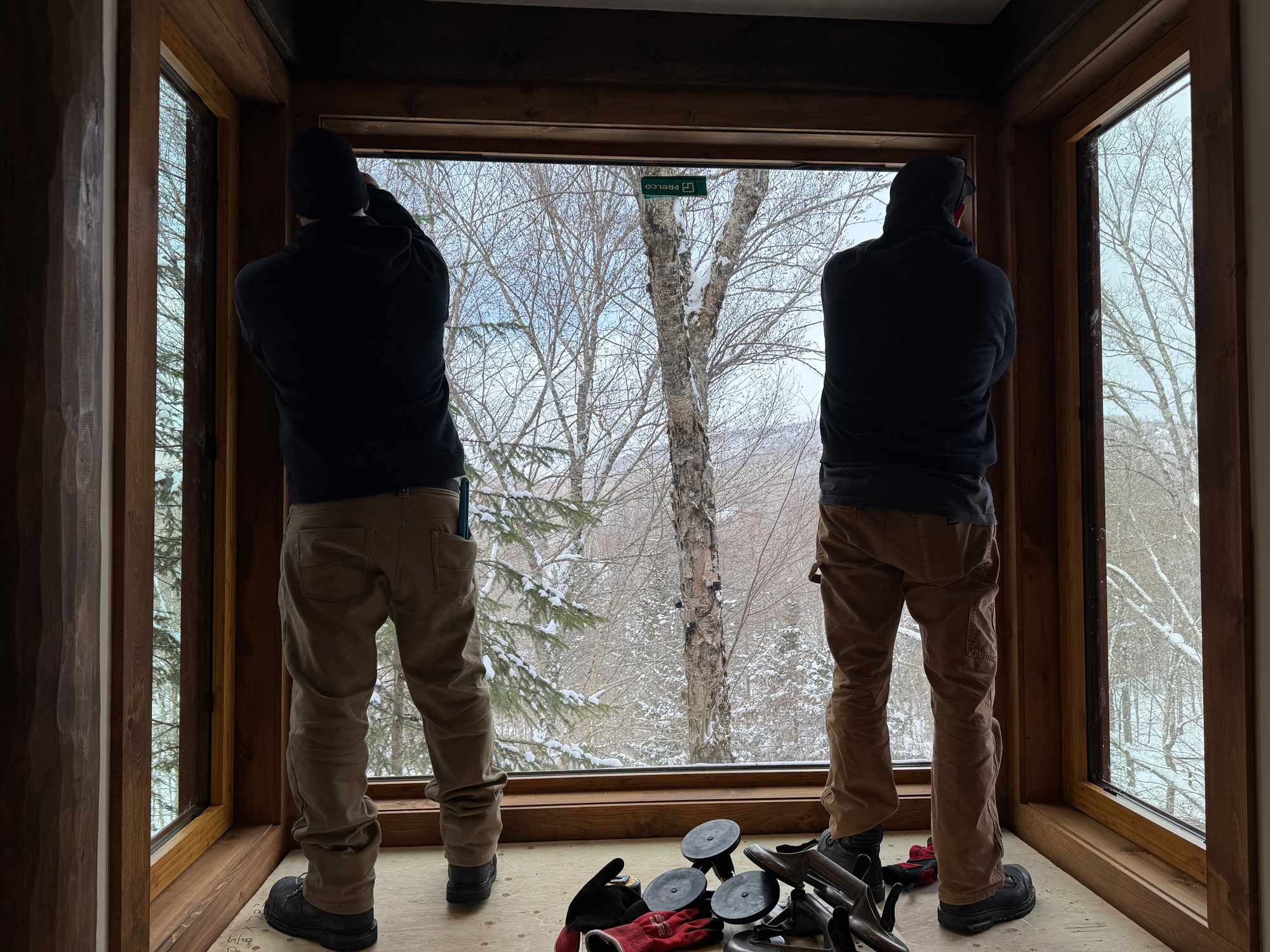 Installation of a large Reynaers Aluminum MasterLine 8 fixed bathroom window flanked by tilt-turn operable units, framing expansive snowy forest views.