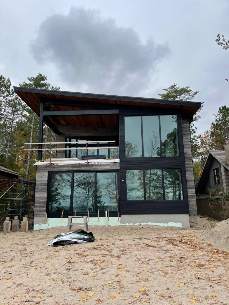 Exterior facade of a Georgian Bay cottage featuring Reynaers Aluminum MasterLine 8 fixed windows, a CP155 sliding door on the lower level, and CF77 folding doors above.