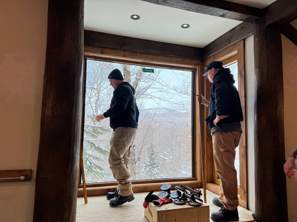 Installers finishing a large Reynaers Aluminum MasterLine 8 fixed bathroom window at a cottage, with expansive glazing framing the snowy forest view.