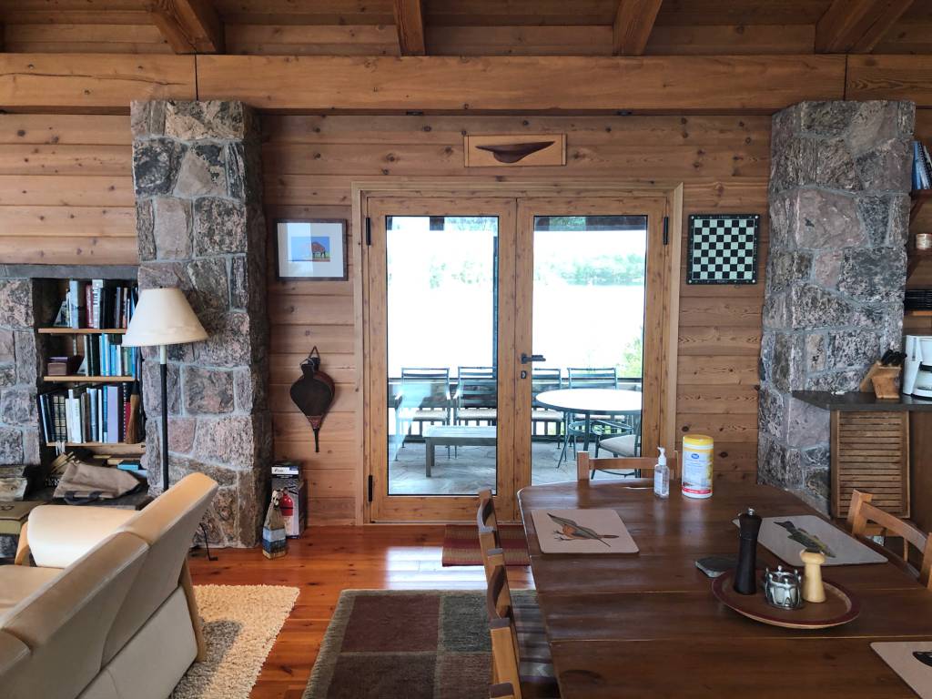Interior of a Georgian Bay island cottage dining area with Reynaers CS77 French doors in wood sublimation finish opening to a covered patio.