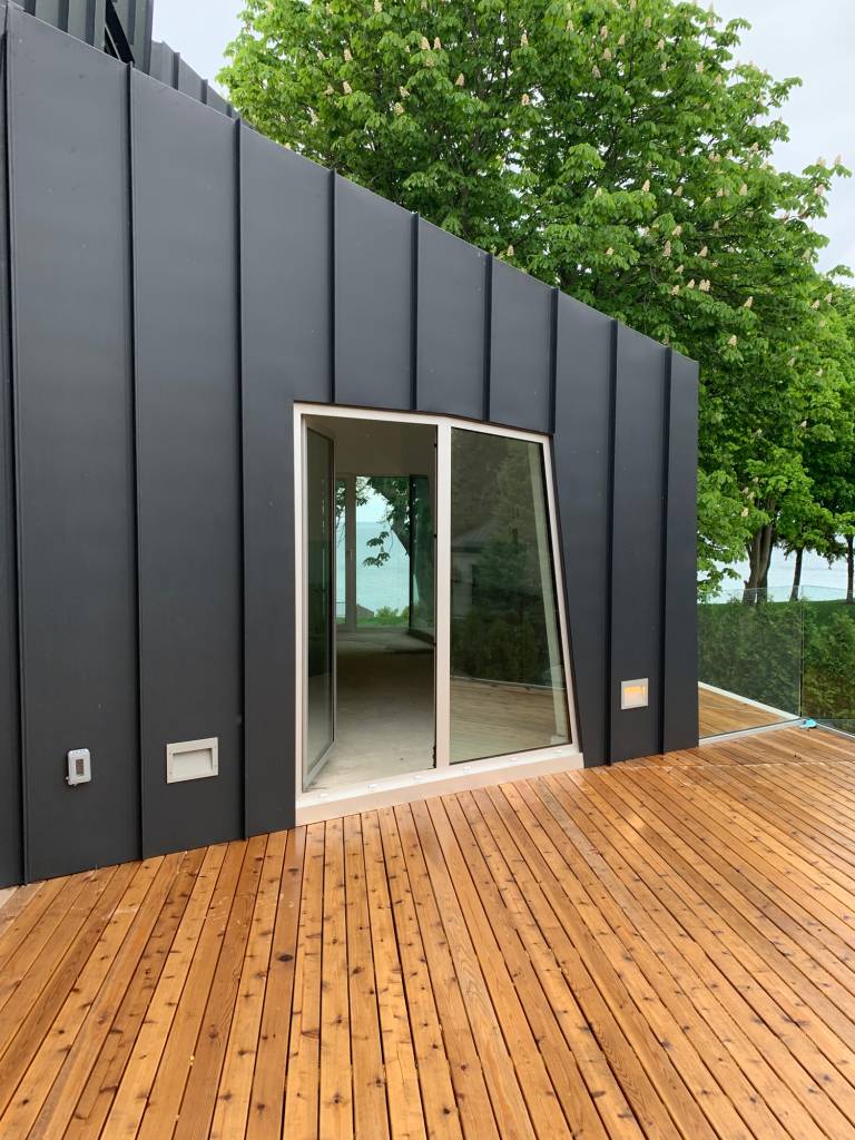 Reynaers CS77 swing door in natural anodized finish leading from a modern angular Sarnia home to the deck.