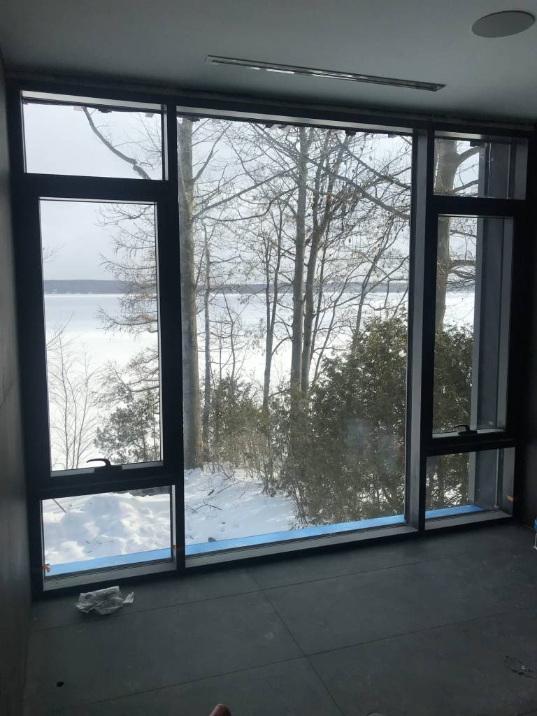 Bedroom view in a Lake Simcoe modern home featuring Reynaers MasterLine 8 fixed glazing with open-out awning style operators overlooking snowy trees.