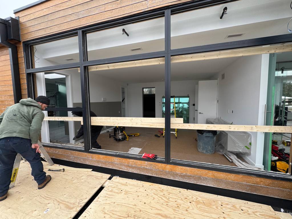 Crew installing Reynaers MasterLine 8 windows in a Muskoka cottage, with black aluminum framing set into a wood-clad exterior wall.