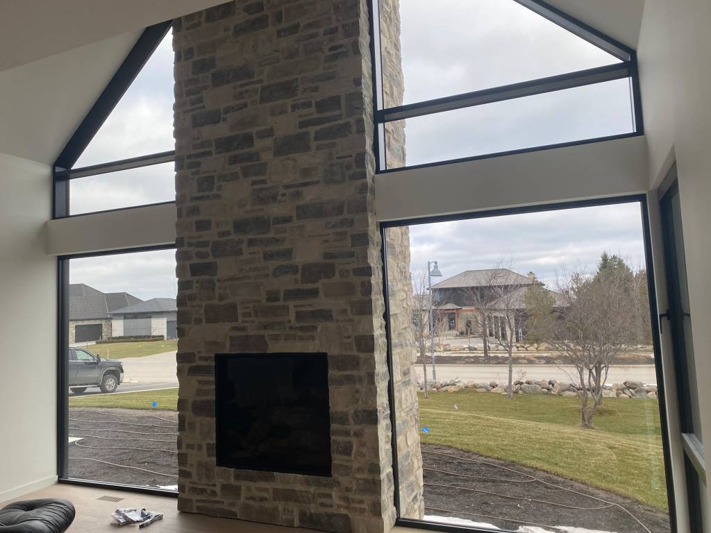 Living room wall of a Blue Mountains modern home with Reynaers SL38 windows installed beneath a raked Reynaers CW50 curtain wall beside a stone fireplace.