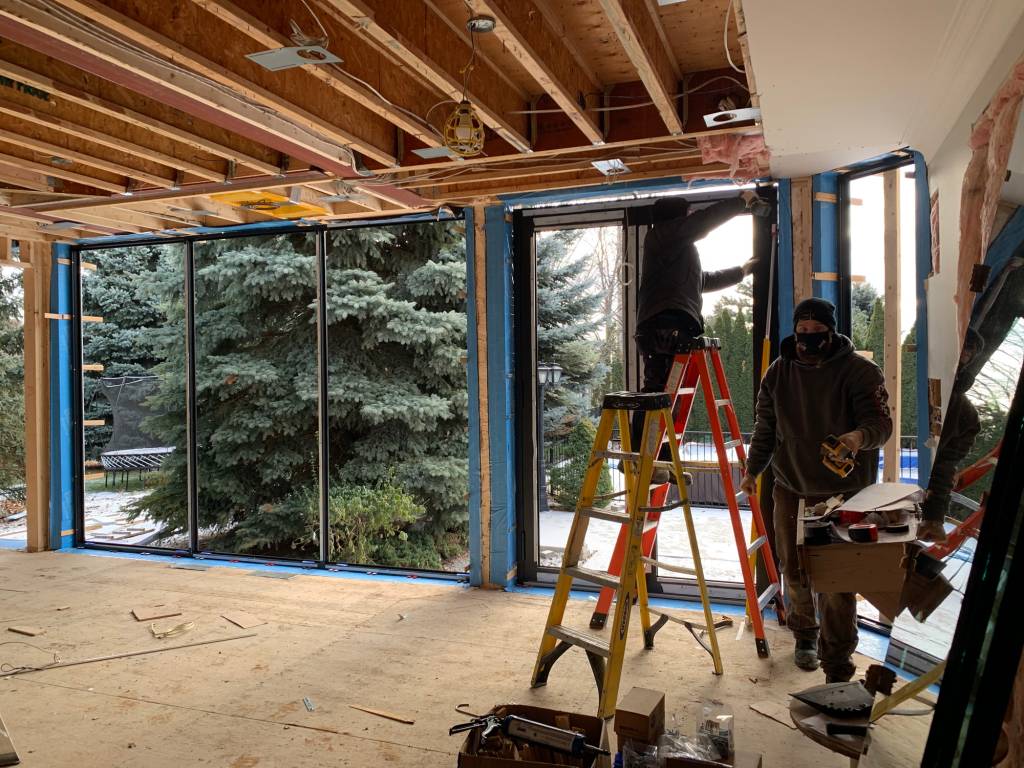 Installation in progress of Reynaers SL38 slim windows and doors at a Barrie luxury home, with large glass openings framing evergreen trees.