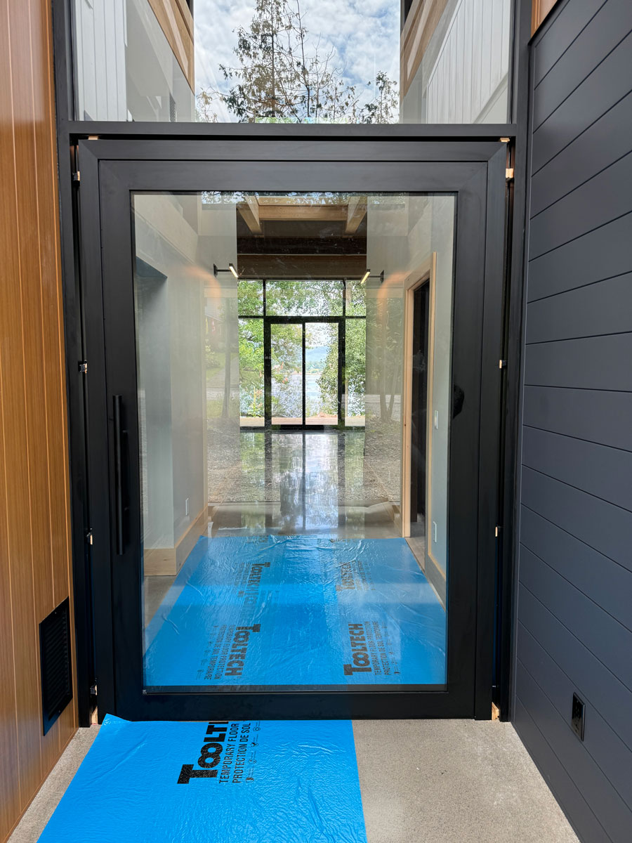 Exterior view of a 4.5' x 7.5' Reynaers MasterLine 8 black pivot door framed in curtain wall with glass above, Ottawa River home near Ottawa.