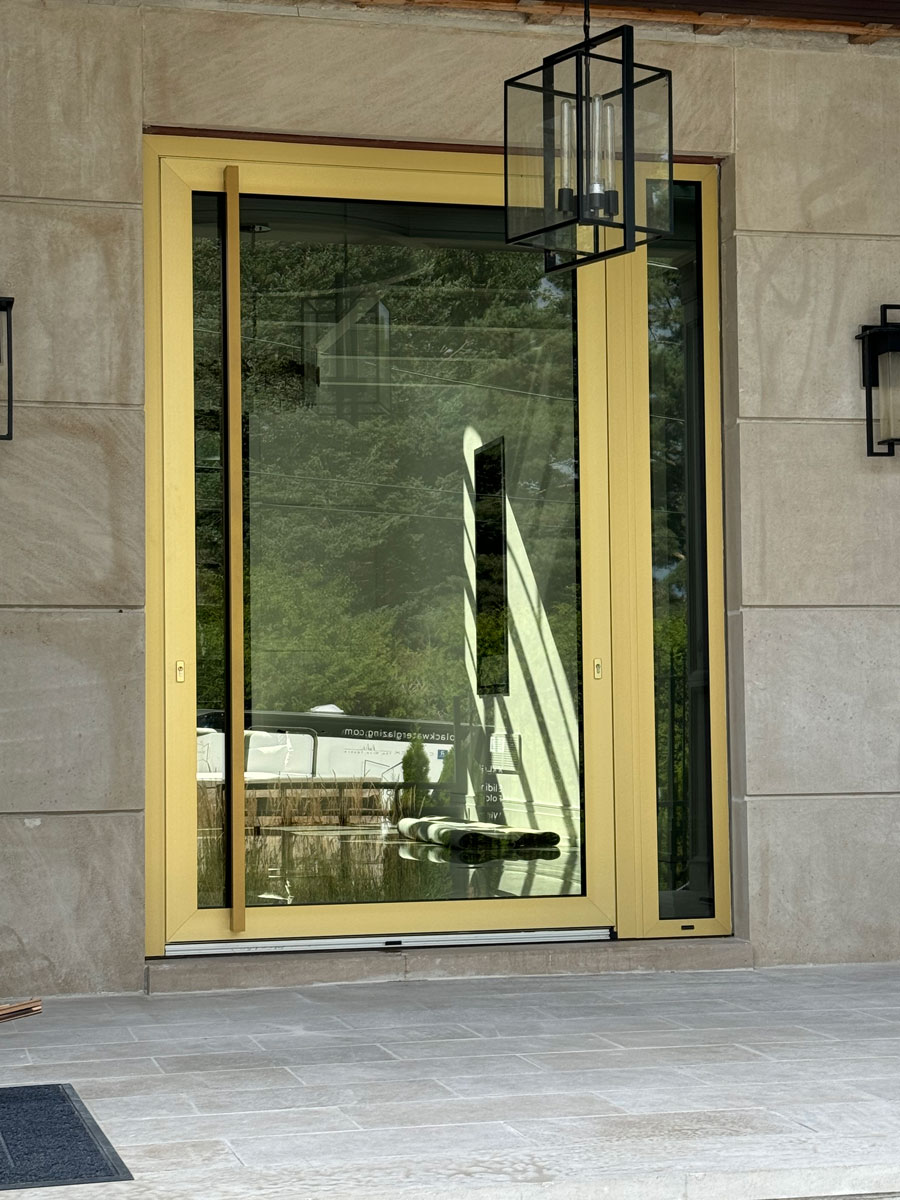 Exterior view of a 4' x 9' Reynaers MasterLine 8 light bronze anodized pivot entry door with 1' sidelight, closed on a Toronto luxury home.