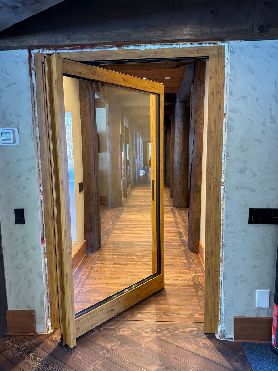 Half-open Reynaers MasterLine 8 interior pivot door in wood sublimation finish with large glass panel, separating the games room from the living area in a Mont-Tremblant home.