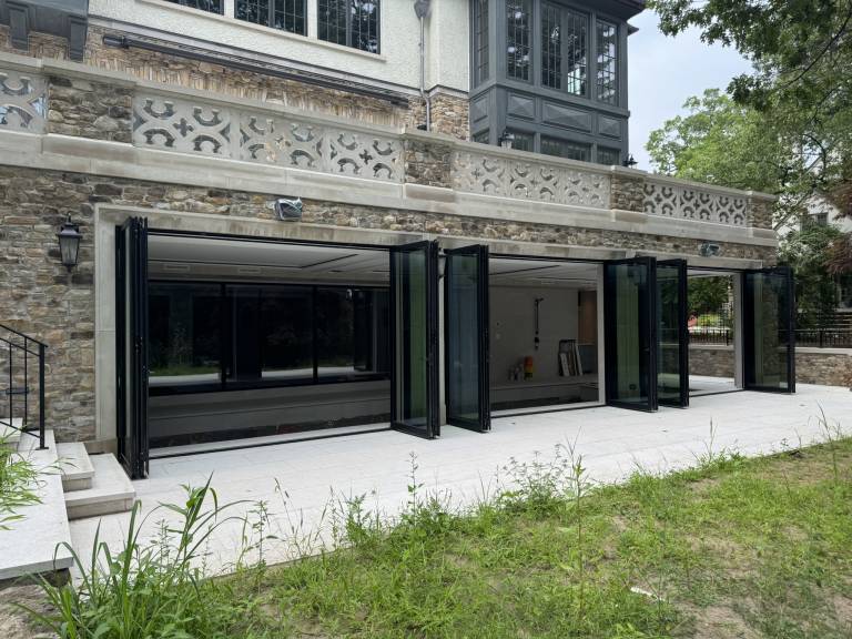Alternate exterior angle showing four Reynaers CF77 black folding doors fully open between the indoor swimming pool and outdoor space of a Toronto luxury residence.
