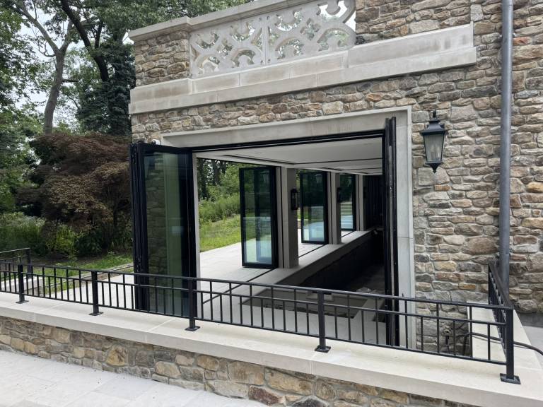 Exterior view of four Reynaers CF77 black folding doors, fully open to connect the indoor swimming pool with the outdoor space of a Toronto luxury residence.