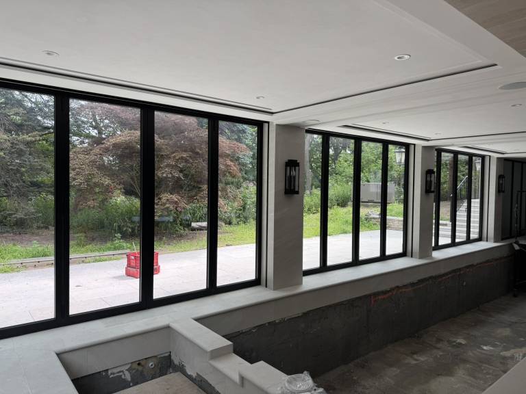Three Reynaers CF77 four-panel black folding doors separating an indoor swimming pool from the outdoor space of a luxury residence in Toronto, ON.